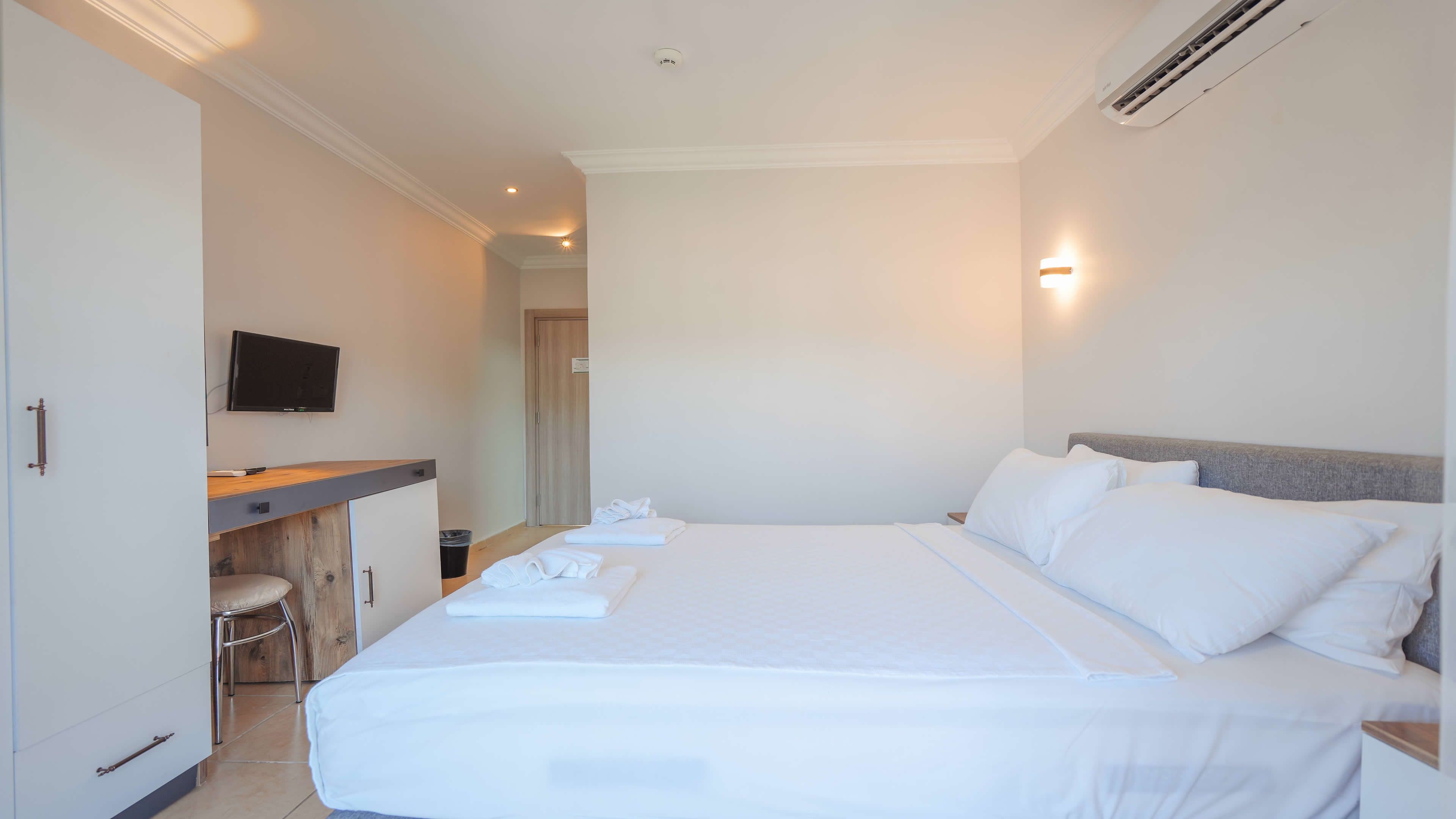 Una habitación de hotel con una cama, un escritorio con una silla, un televisor y un aire acondicionado instalado en la pared.