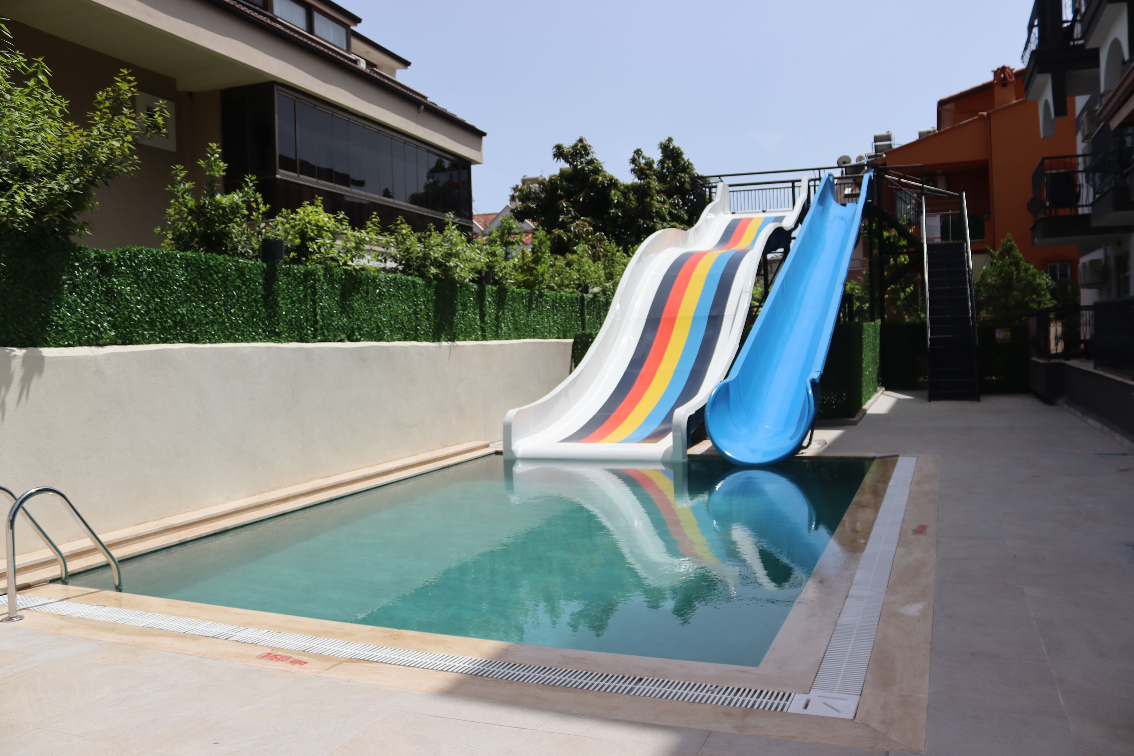 Piscina com dois toboáguas, rodeada por um muro baixo e vegetação.