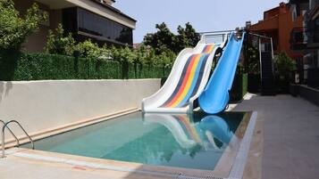 Piscina com dois toboáguas, rodeada por um muro baixo e vegetação.