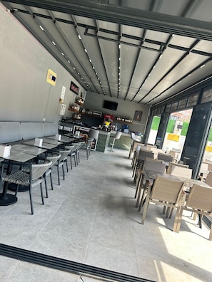 Un restaurante con zona de bar, asientos con mesas y sillas, y una barra con carta.