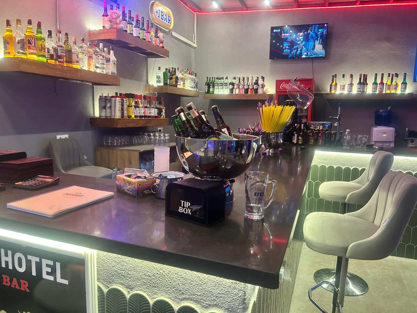 Zona de bar con estantes de botellas de licor, un cubo de hielo grande y taburetes de bar.