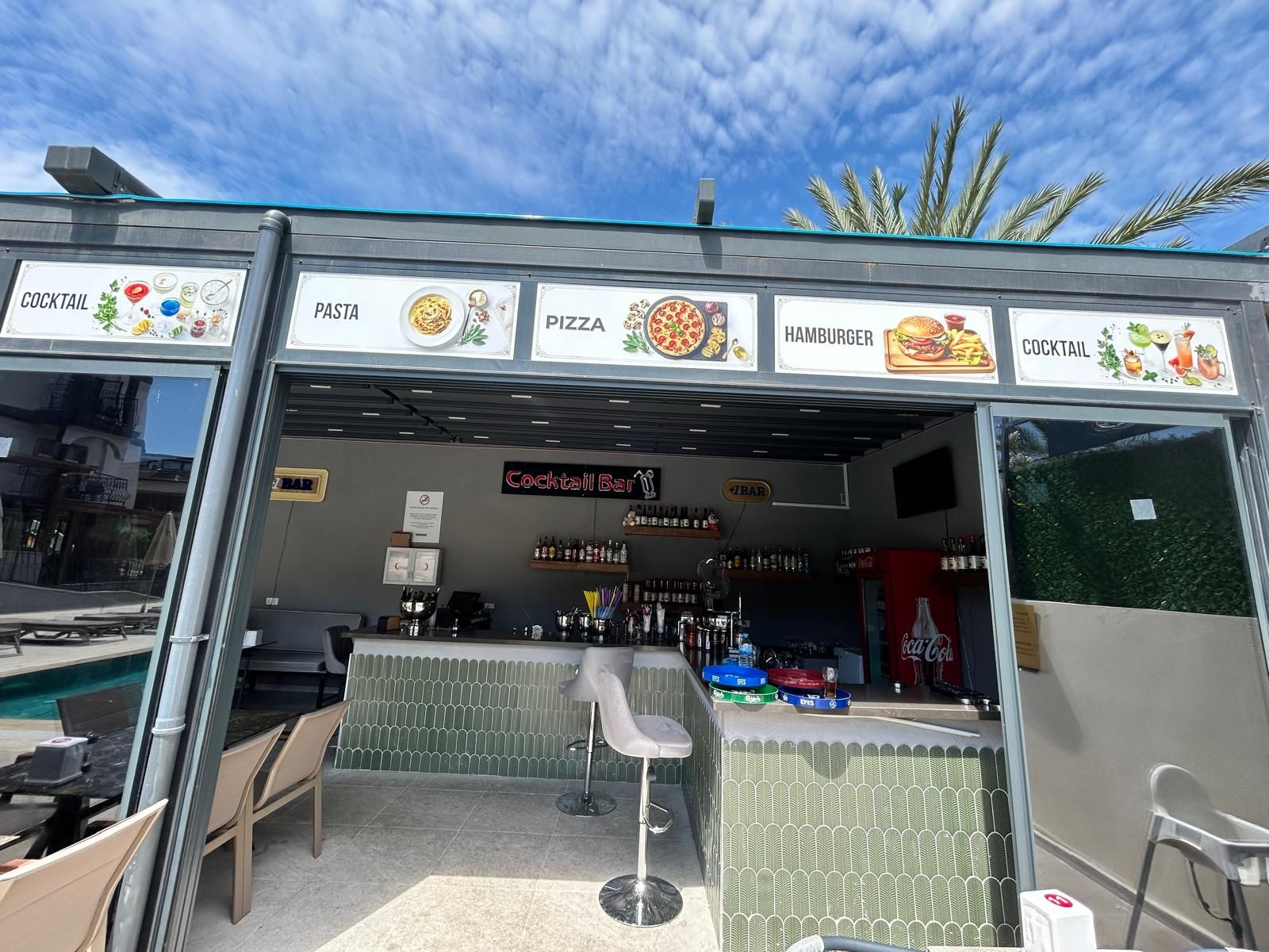 Un bar con un panel de menú que muestra opciones como cócteles, pasta, pizza y hamburguesas.