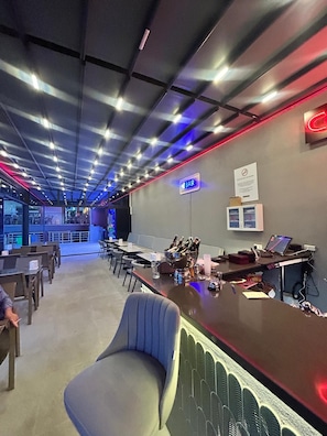 Zona de bar con un letrero de neón, barra y área de estar con mesas y sillas.