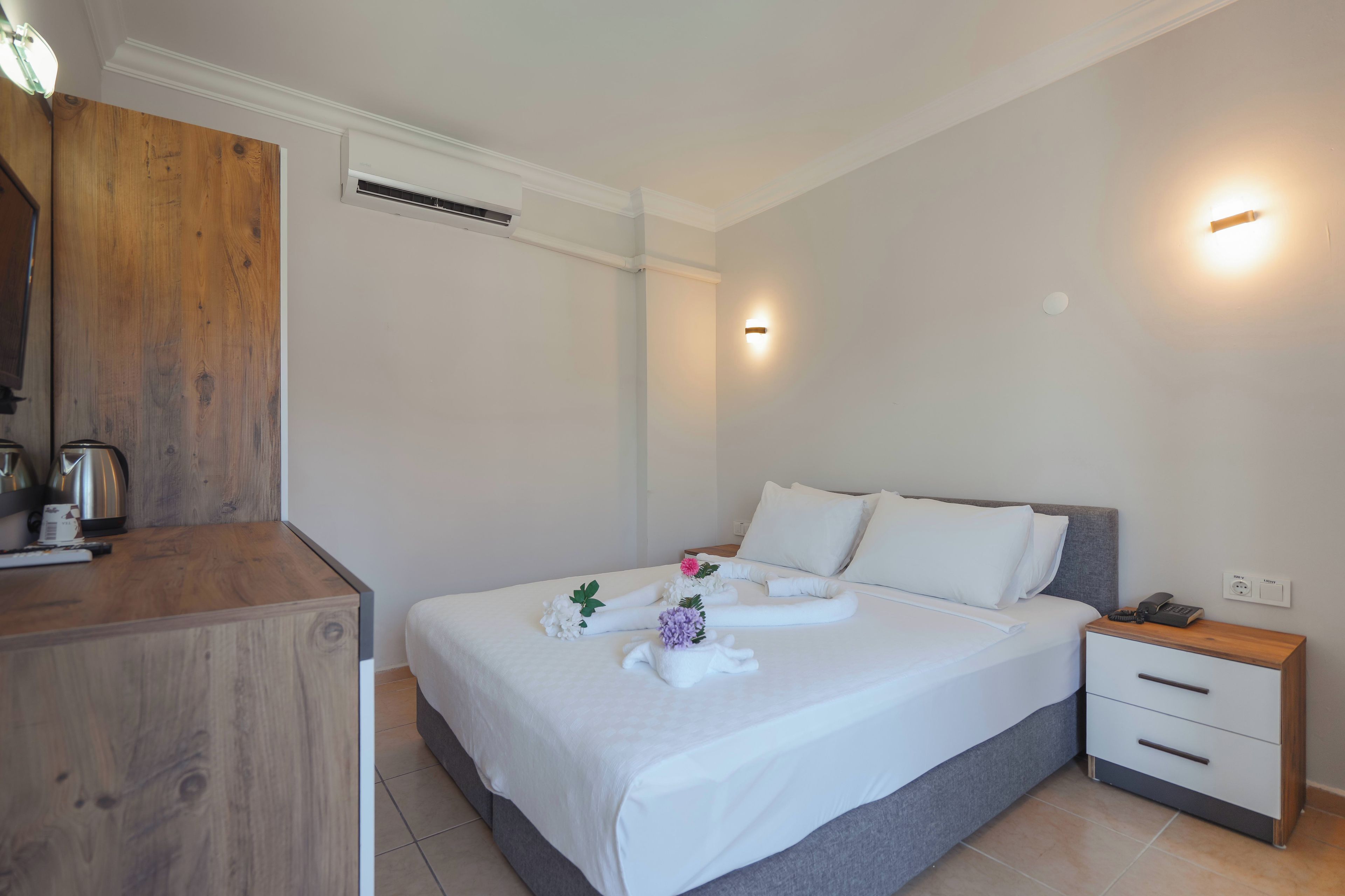 Een hotelkamer met een bed, nachtkastje en een houten bureau met een waterkoker.