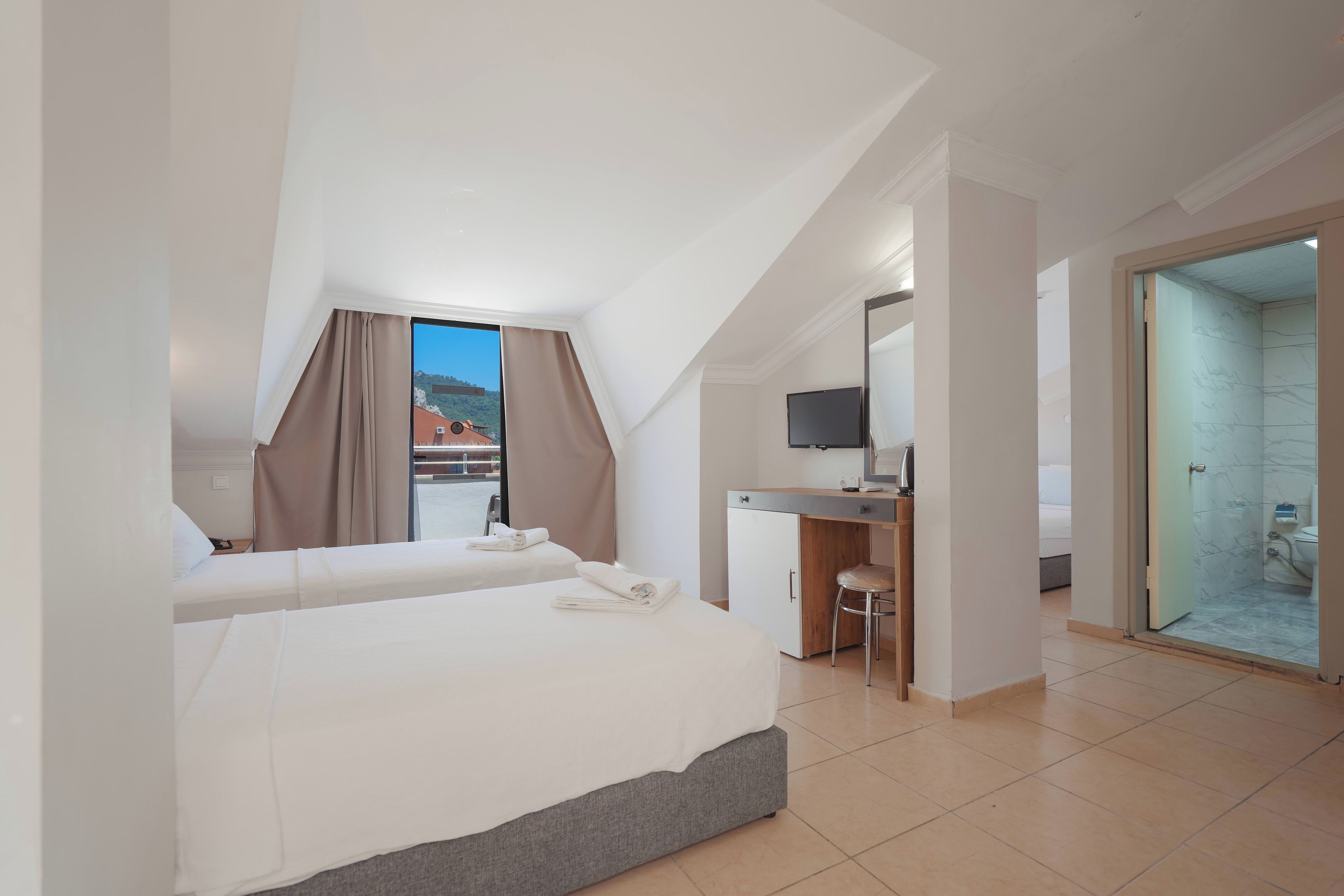 Een hotelkamer met twee bedden, een bureau, een televisie en een badkamer met een glazen deur.