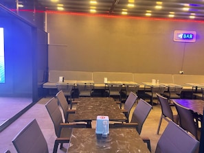 Una sala de conferencias con mesas, sillas, un cartel que dice 'BAR' y una pantalla de proyección.