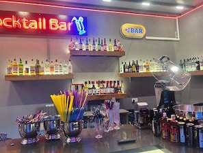 Zona de bar con estantes llenos de botellas de licor, un letrero de neón y una máquina de café.