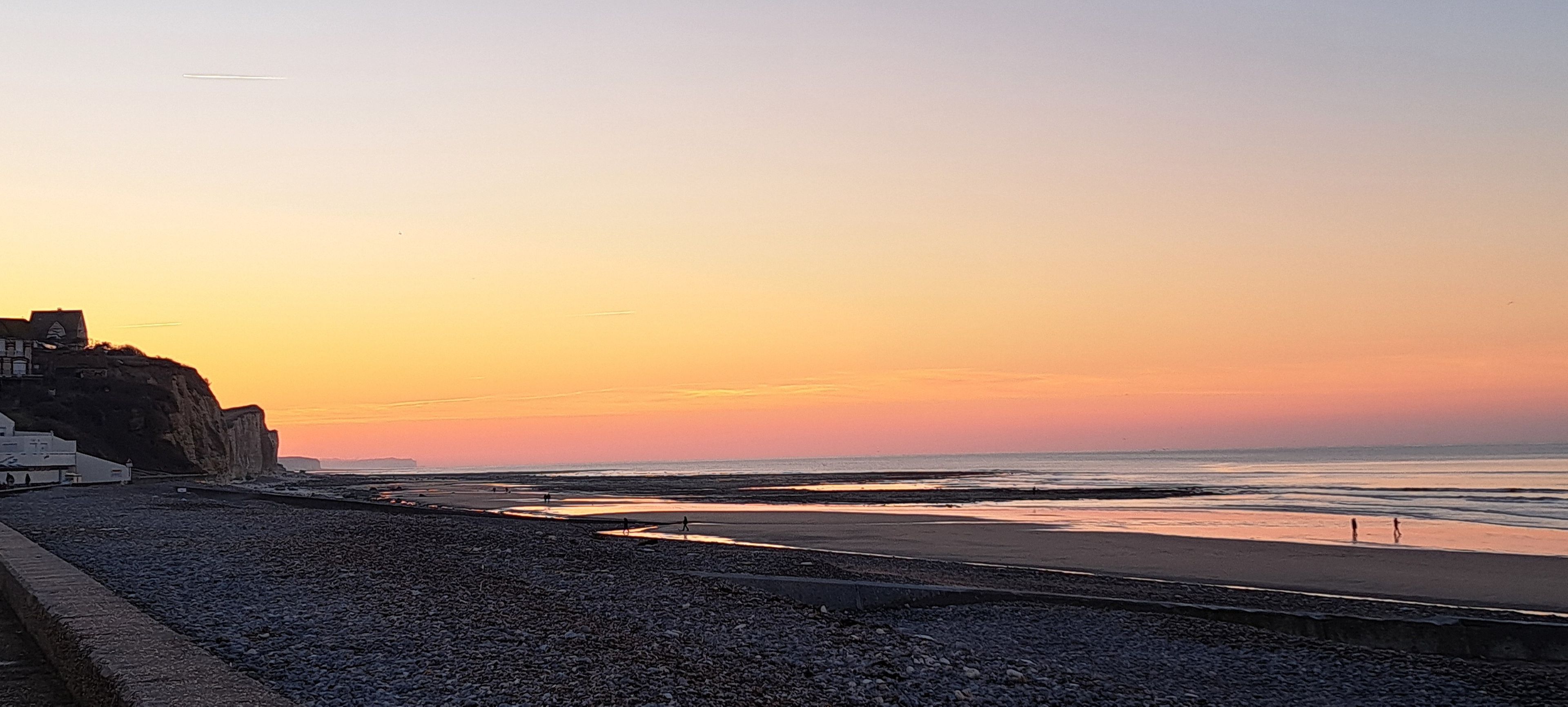 Eine Küstenlandschaft mit felsigem Strand, ruhiger See und einem Sonnenuntergangshimmel.