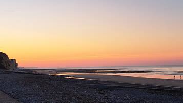 Eine Küstenlandschaft mit felsigem Strand, ruhiger See und einem Sonnenuntergangshimmel.