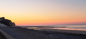 Eine Küstenlandschaft mit felsigem Strand, ruhiger See und einem Sonnenuntergangshimmel.