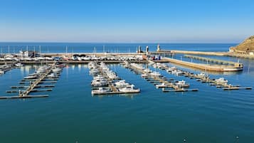 Een jachthaven met talloze boten afgemeerd in kalm water, een steiger die zich uitstrekt over de zee, en een heuvelachtig landschap op de achtergrond.