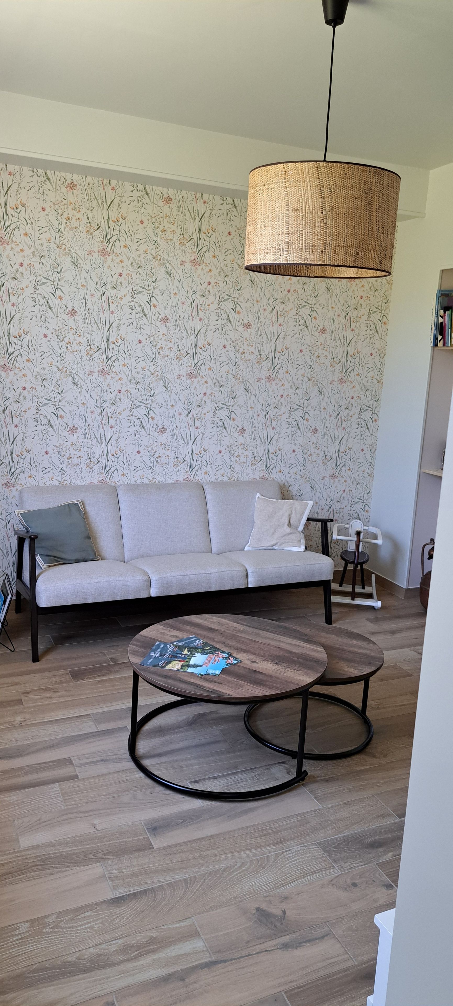 Un salon comprenant un canapé, une table basse, un luminaire suspendu et un papier peint à motifs.