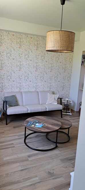 A living room with a sofa, a coffee table, a hanging light fixture, and a patterned wallpaper. - Holiday Home 'La Parenthèse Cauchoise' with Sea View, Comfort and Tranquility (Malleville-les-Grès)