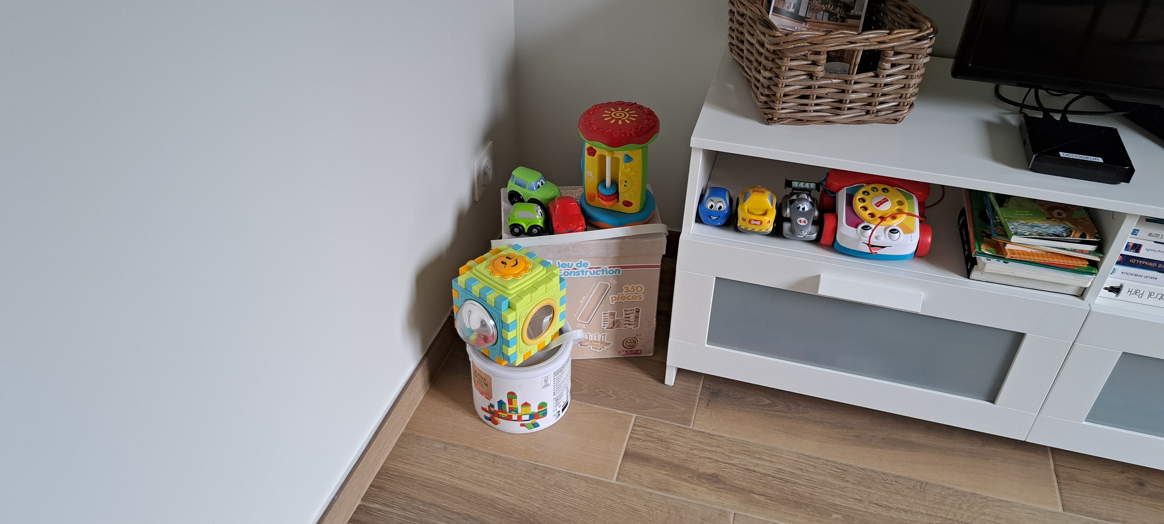 Un espace de jeux pour enfants avec des jouets, un bac de rangement et un meuble blanc contenant des livres.