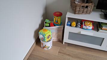 Un espace de jeux pour enfants avec des jouets, un bac de rangement et un meuble blanc contenant des livres.