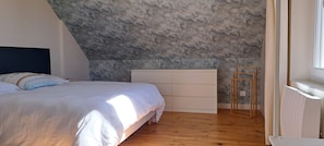 Ein Schlafzimmer mit schrägem Dach, einem Bett mit weißer Bettdecke, Holzboden und einem Fenster auf der rechten Seite.