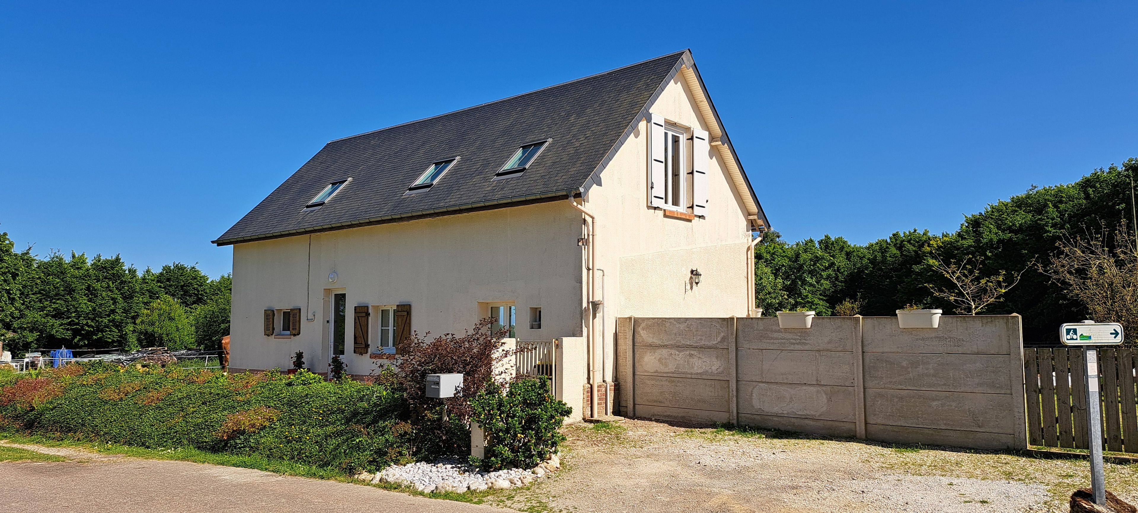Ein zweistöckiges Haus mit einem geneigten Dach, einem umzäunten Garten und einer Schotterauffahrt.