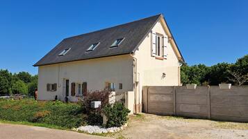 Ein zweistöckiges Haus mit einem geneigten Dach, einem umzäunten Garten und einer Schotterauffahrt.