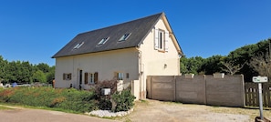 Ein zweistöckiges Haus mit einem geneigten Dach, einem umzäunten Garten und einer Schotterauffahrt.