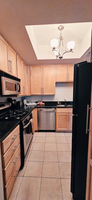 A kitchen with wooden cabinets, a black refrigerator, a stainless steel dishwasher, and a gas stove. - Luxury Las Vegas Strip!  1BR Private Residences Condo ~ 24/7 Pool 2-09 (Las Vegas)