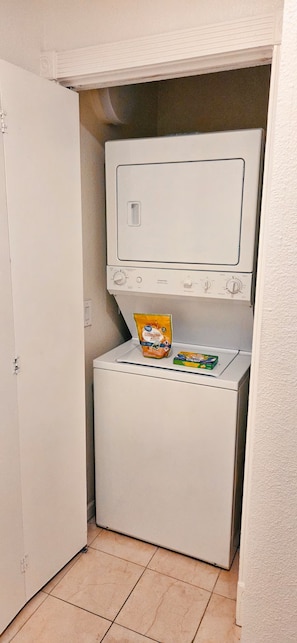 A compact laundry room with a washing machine and dryer, a door, and a bag of laundry on the dryer. - Luxury Las Vegas Strip!  1BR Private Residences Condo ~ 24/7 Pool 2-09 (Las Vegas)