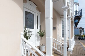 Un bâtiment blanc doté d’un balcon, une porte portant l’inscription « Paragon House 1904 » et une petite plante en pot.