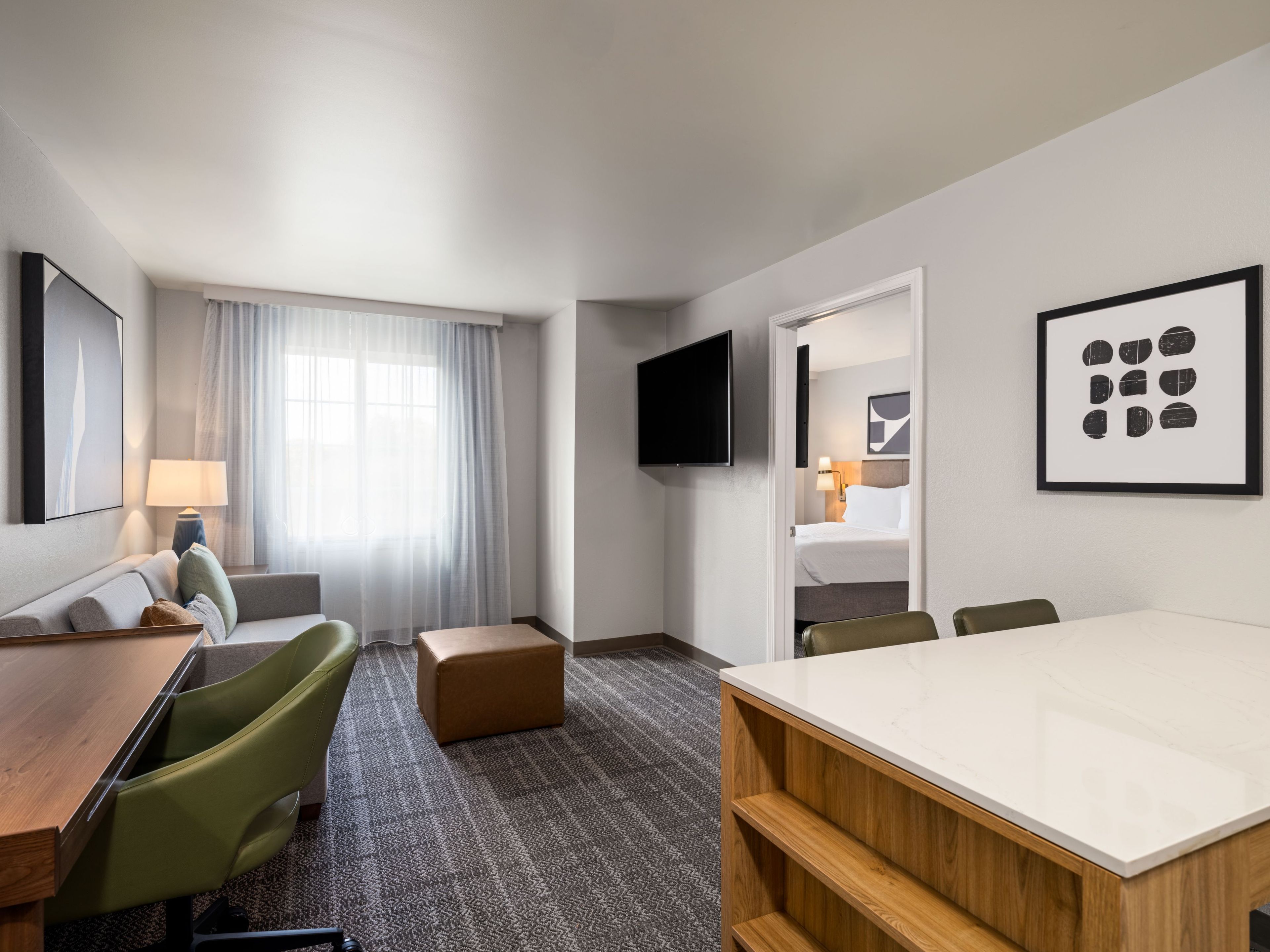 A hotel room with a bed, a desk, a chair, a TV, and artwork on the walls.