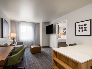 A hotel room with a bed, a desk, a chair, a TV, and artwork on the walls.