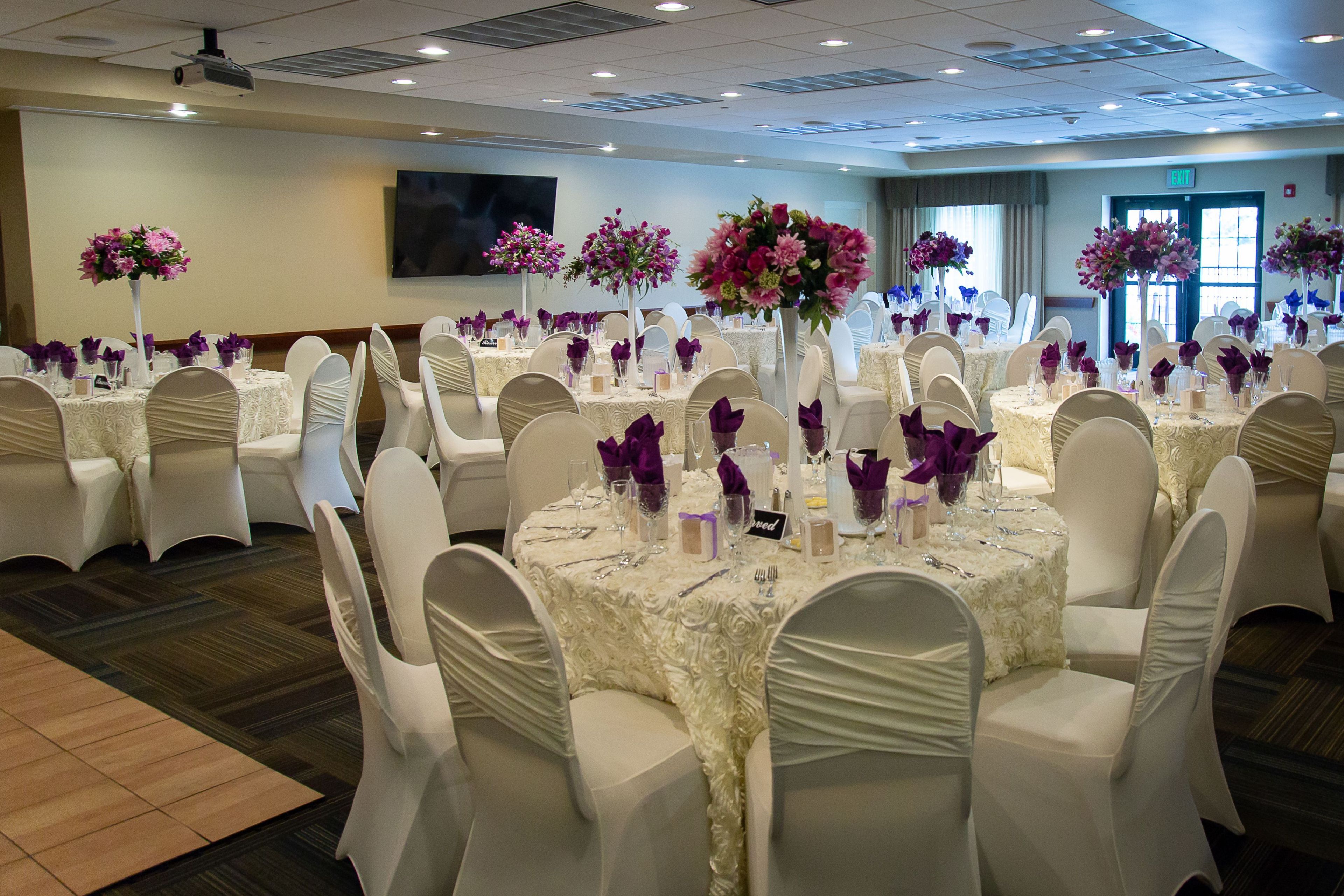 A banquet hall with round tables, white chairs, and floral centerpieces.