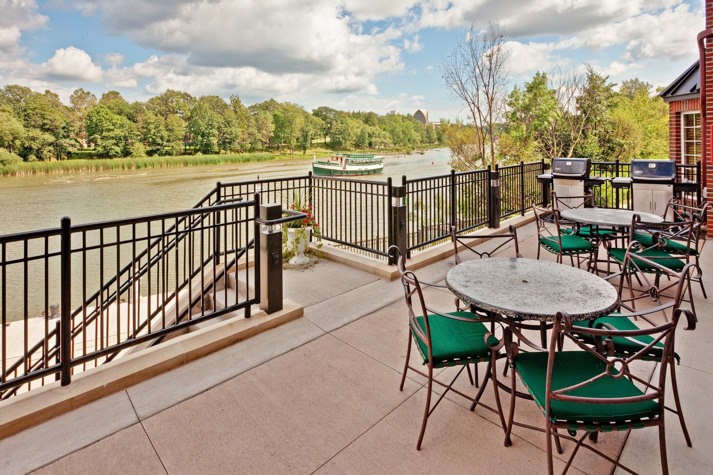 An outdoor patio with tables and chairs, a river view, and a boat on the river.