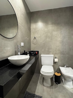 A modern bathroom with a large round mirror, a white sink, a toilet, and a bidet. - Hermo Studio, 2 meters from the MOVISTAR ARENA - Palermo Queens (Buenos Aires)