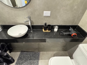A modern bathroom with a white sink, black countertop, and a hairdryer on the right. - Hermo Studio, 2 meters from the MOVISTAR ARENA - Palermo Queens (Buenos Aires)
