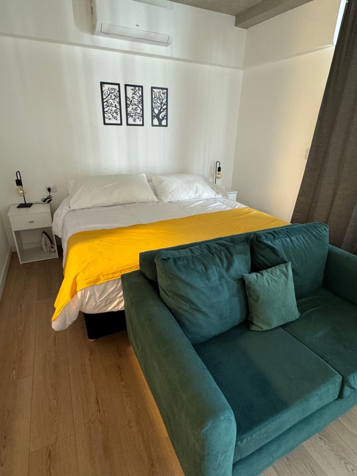 A bedroom with a bed, a nightstand, a lamp, and a green sofa.