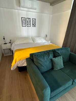 A bedroom with a bed, a nightstand, a lamp, and a green sofa. - Hermo Studio, 2 meters from the MOVISTAR ARENA - Palermo Queens (Buenos Aires)