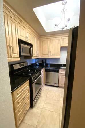 A kitchen with light wooden cabinets, a black countertop, stainless steel appliances, and a skylight. - Luxury Las Vegas Strip!  1BR Private Residences Condo ~ 24/7 Pool 2-18 (Las Vegas)