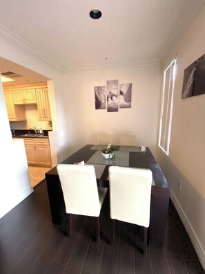 A dining area with a dark wood table, two white chairs, and a vase with a plant. There are three framed pictures on the wall above the table. - Luxury Las Vegas Strip!  1BR Private Residences Condo ~ 24/7 Pool 2-18 (Las Vegas)