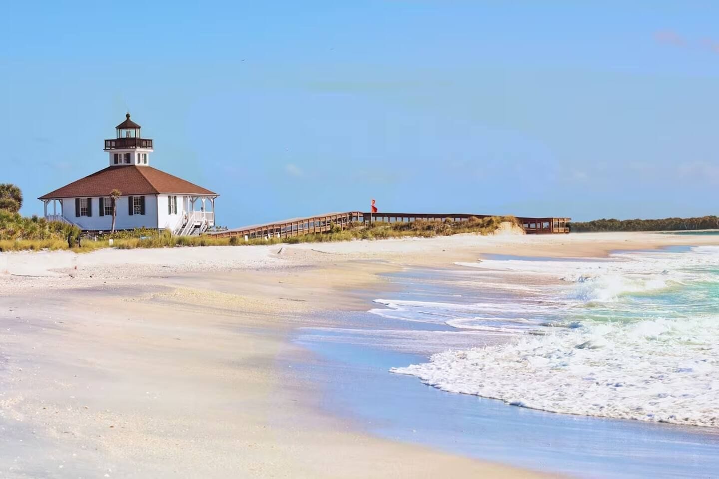 A beach with a white building and a pier extending into the water.