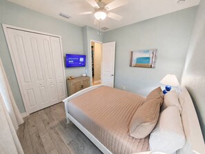 A bedroom with a bed, a ceiling fan, a television, and a door leading to another room. - Heated Saltwater Pool | Near Beach | Pets Welcome! (Rotonda West)