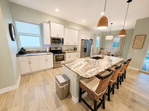 A modern kitchen with white cabinets, a marble island, and a dining area with wicker chairs. - Heated Saltwater Pool | Near Beach | Pets Welcome! (Rotonda West)