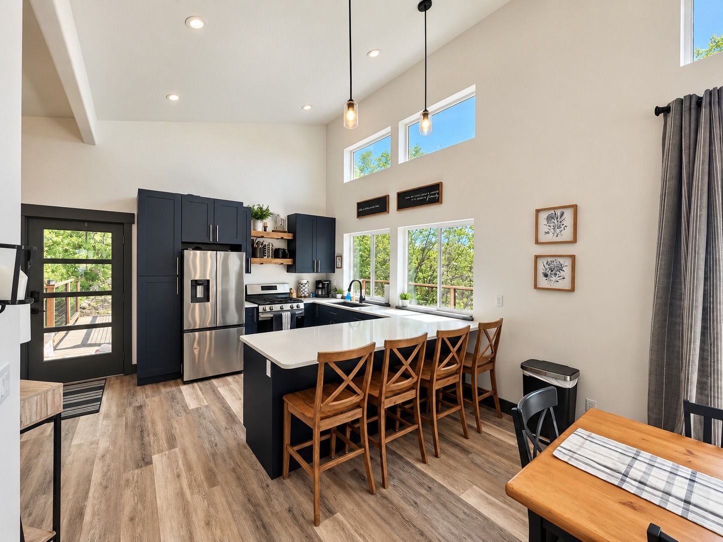 Une cuisine moderne dotée d’un îlot central, de meubles de rangement aux couleurs sombres, d’appareils électroménagers en acier inoxydable et d’un coin repas avec des chaises en bois.