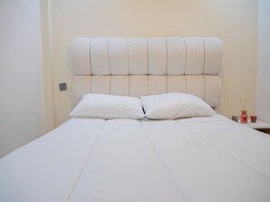 Ein Bett mit einer gesteppten Kopflehne, zwei Kissen und einem Nachttisch mit Kerze und kleiner Aufbewahrungsbox.
