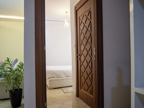 Ein Durchgang zu einem Schlafzimmer mit einem Bett, einer Topfpflanze und einer Deckenleuchte.