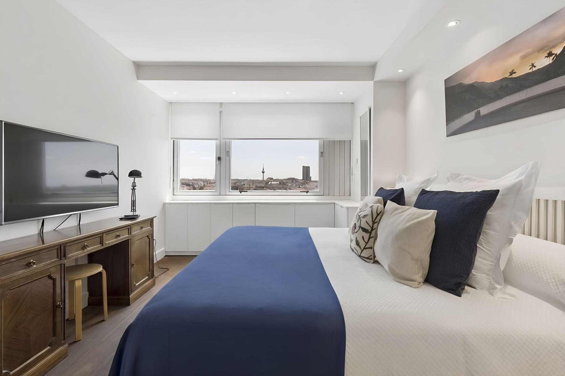 Et moderne hotelværelse med en stor seng, et fladskærms-tv, et skrivebord og et vindue med udsigt over byen.