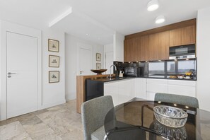 A modern kitchen with a dining area, featuring a glass table, chairs, and a wooden cabinet above the stove. - Elegant 1BR in Prime Colón Madrid (Madrid)