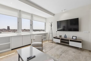A modern living room with a large window, a flat-screen TV, a coat rack, and a minimalist design. - Elegant 1BR in Prime Colón Madrid (Madrid)