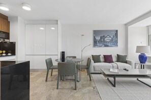 A modern living room with a sofa, coffee table, and chairs. There is a dining area with a table and chairs. A large window provides a view of the city. - Elegant 1BR in Prime Colón Madrid (Madrid)