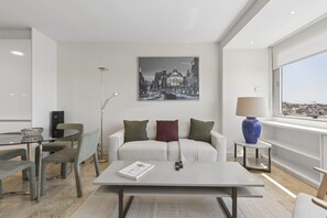 A modern living room with a sofa, coffee table, and a cityscape painting on the wall. - Elegant 1BR in Prime Colón Madrid (Madrid)