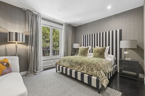 Une chambre moderne avec un grand lit, deux lampes de chevet, une vue sur la verdure et un tapis à motifs.
