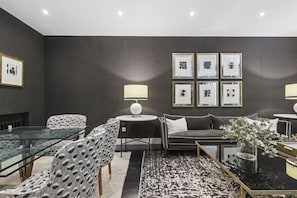 Ein modernes Wohnzimmer mit einem Glastisch, gemusterten Stühlen, einem grauen Sofa und gerahmten Kunstwerken an der Wand.