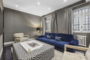 Un salon moderne avec un canapé bleu, un pouf à motifs et un fauteuil beige.
